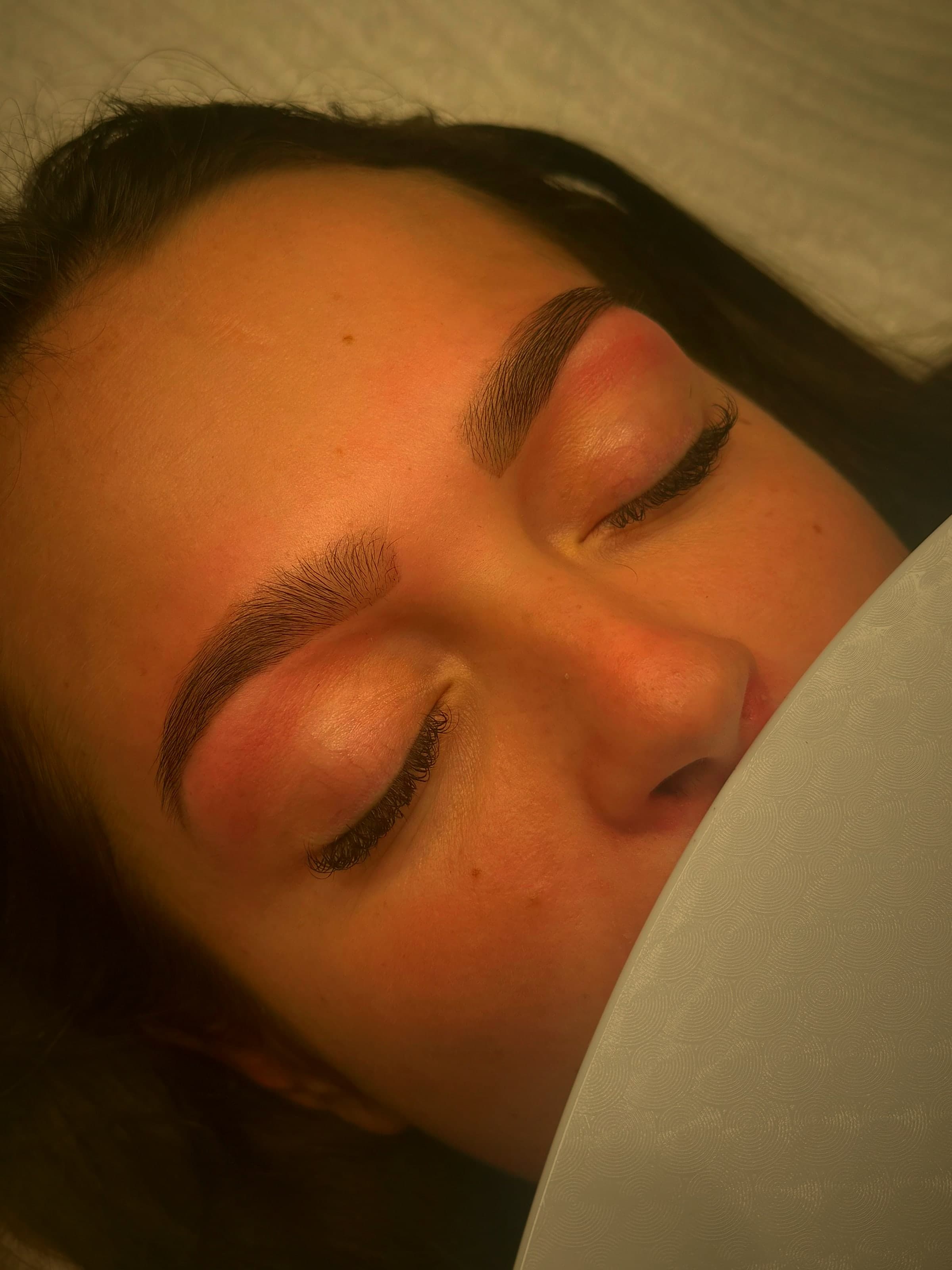Close-up of freshly laminated brows and lash extensions in warm light